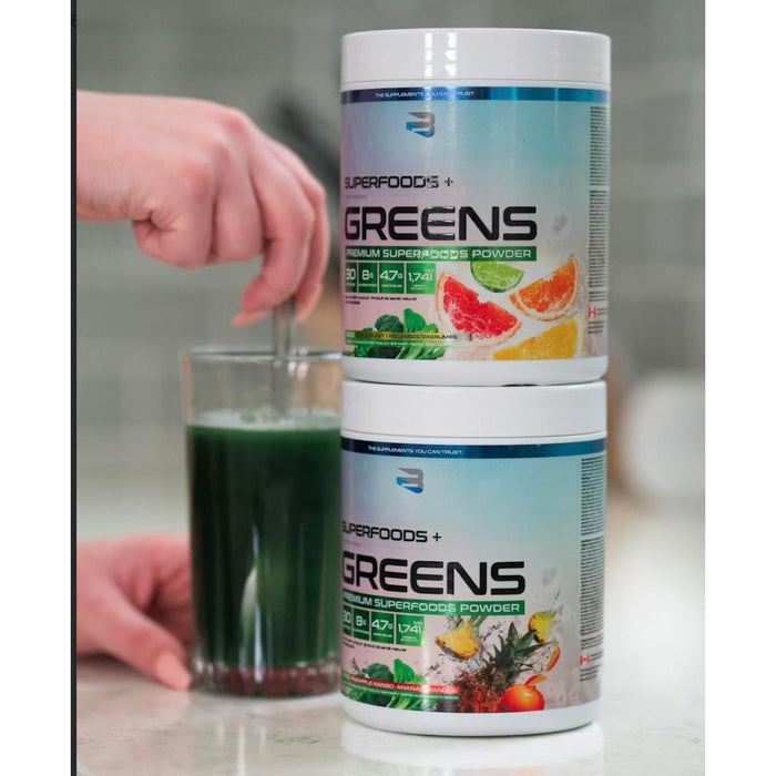 Believe Supplements Greens — two Superfoods+ tubs stacked beside a glass of green drink, greens in Canada
